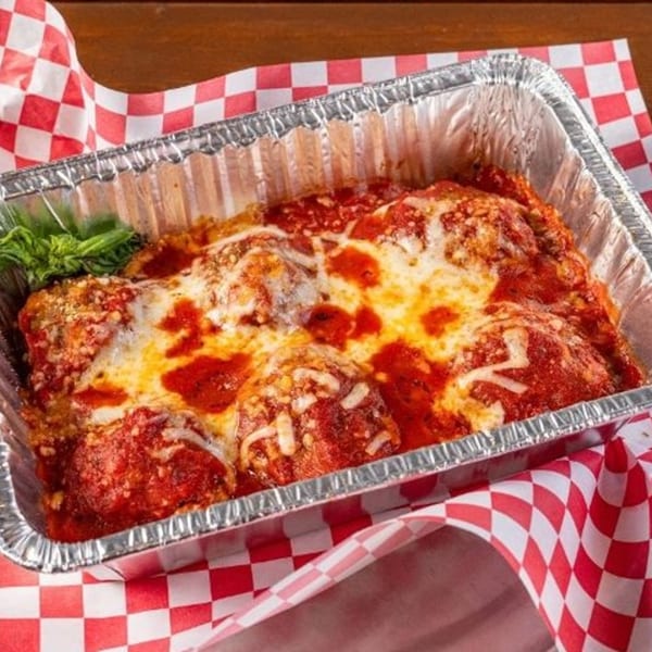 Baked ziti or lasagna with melted cheese and red sauce in a foil pan on a checkered napkin.