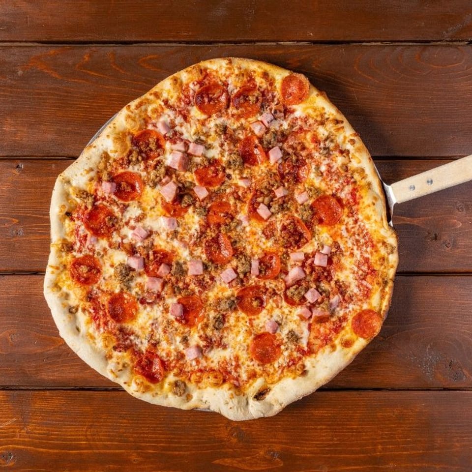 A New York Pizza Pub pizza with pepperoni, sausage, and ham on a wooden table.