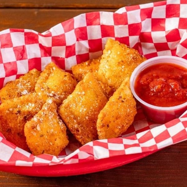 Golden fried ravioli with parmesan cheese and a side of marinara sauce in a red checkered basket.
