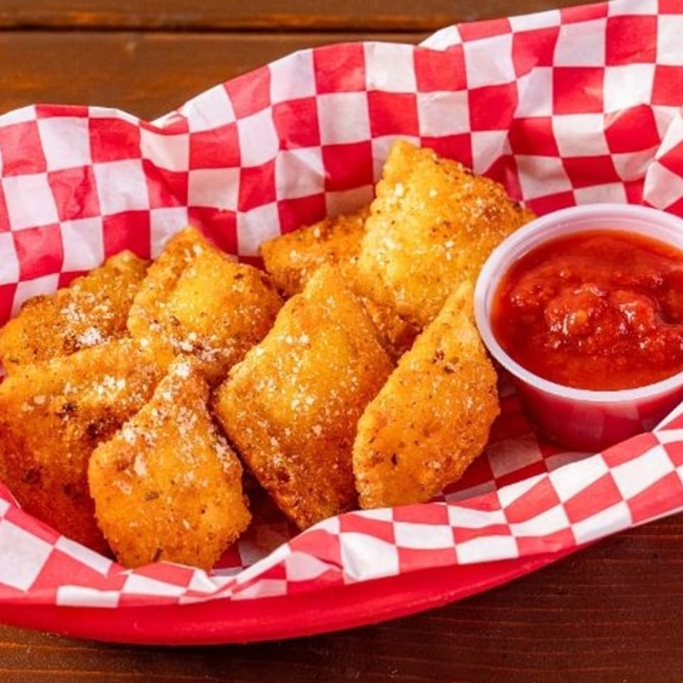 Golden fried ravioli with parmesan cheese and a side of marinara sauce in a red checkered basket.