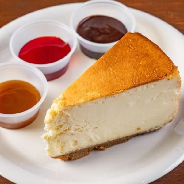 A slice of New York cheesecake with three dipping sauces: caramel, raspberry, and chocolate.