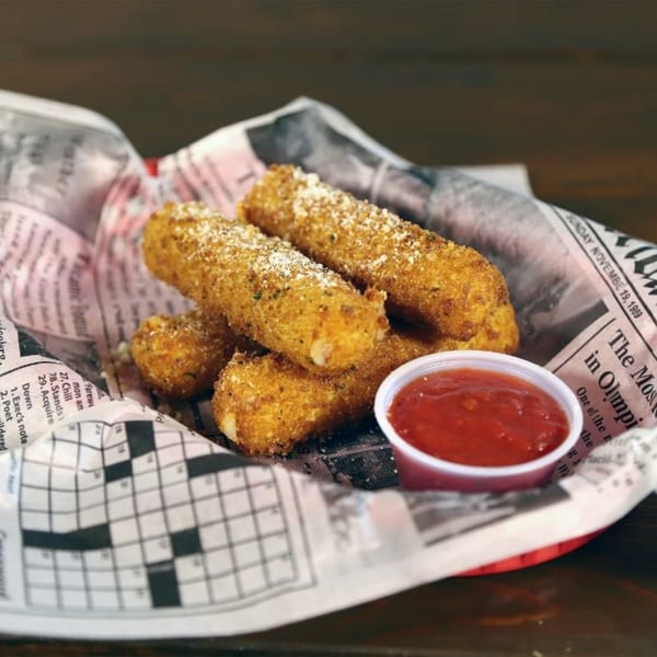 Golden-brown mozzarella sticks with parmesan, served in a newspaper-lined basket with marinara sauce.